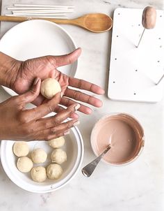 two hands reaching for some kind of food on a plate with spoons and utensils