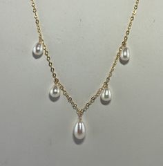 This is a freshwater pearl necklace with 5 teardrop shaped pearls dangling from an 18" gold-filled chain.  The pearls are white with a slight pink secondary color.  They measure 6-6.5mm in diameter and 9-11mm in length.  I've put the largest in the center with the smaller pearls graduating up on the sides.    The 1.7mm gold-filled, curb link chain is finished with a spring ring clasp.  This would be lovely as a wedding necklace or for any other occasion. This comes gift boxed and ships free USPS First Class.  If you'd like faster shipping you can upgrade to Priority Shipping at checkout for $5.50. Thank you for viewing. Pear-shaped Pearl Drop Necklaces, White Long Drop Necklace With Pearl, Gold Teardrop Pearl Drop Necklace, Formal Teardrop Pearl Chain Drop Necklace, Pearl White Drop Necklace With Pearl Chain, Gold Teardrop Pearl Necklace, White Dangle Drop Necklace For Formal Occasions, Gold Drop Necklace With Pearl Chain, White Drop Necklace For Anniversary