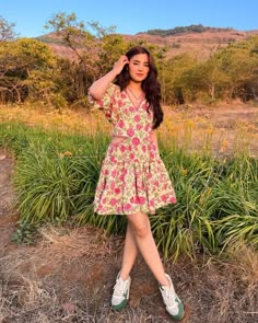 a woman in a floral dress poses for the camera with her hand on her head