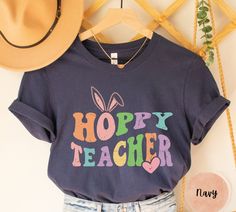 Teacher Easter Shirt, Hoppy Teacher T shirt,Bunny Teacher Gift,Happy Easter Cute Teacher Shirt,Funny Teacher Tee,Peeps Shirt,Easter Day Gift ooooooooooooooooooo ⚠️Important Note: We offer two different shirt brands for your convenience, Bella Canvas and Gildan Soft Style. If you have a preference for a specific brand, please kindly ask us for availability before placing your order. We want to ensure you get exactly what you love! 📦 Brand Availability: If you do not specify a preference, we will Easter Graphic Print Playful Tops, Playful Easter Tops With Graphic Print, Cute Spring Tops With Funny Text, Fun Cotton Tops For Easter, Playful Bunny Design Tops For Spring, Cute Spring Shirt With Funny Text, Spring Funny T-shirt With Text, Cute Shirt With Funny Text For Spring, Cute Graphic Print Tops For Easter