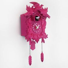 a pink cuckoo clock hanging from the side of a wall in front of a white background