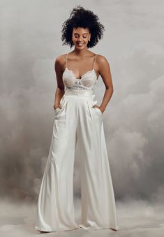 a woman in white pants and bra top posing for a photo with clouds behind her