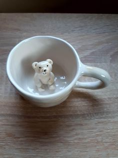 a small white teddy bear sitting in a coffee cup on top of a wooden table