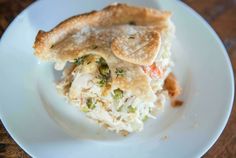 a piece of chicken pot pie on a white plate with a wooden table in the background