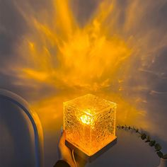 a person holding up a lit cube in front of a yellow light that is shining