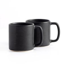 two black coffee mugs sitting next to each other on a white surface with no one around them