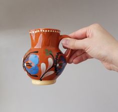 a hand holding a ceramic cup with designs on the outside and inside, in front of a gray background