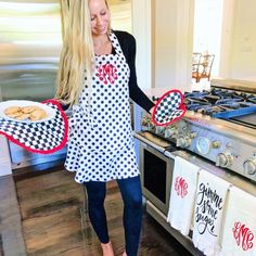 a woman in an apron holding two trays with cookies on them and standing next to the stove