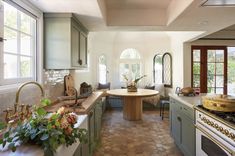 a kitchen with green cabinets and an island in the middle, surrounded by potted plants