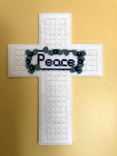 a cross with the word peace on it hanging from a wall in front of a yellow wall