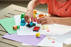 a young boy playing with toys on top of some paper and colored blocks in front of him