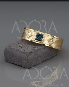 two gold rings with blue and white diamonds sitting on top of a rock next to a stone