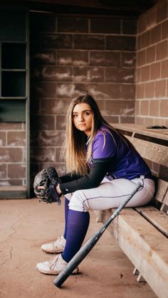 a woman sitting on top of a bench holding a baseball bat and wearing a catchers mitt