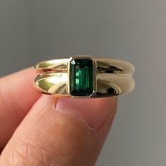 a close up of a person's hand holding a ring with an emerald stone