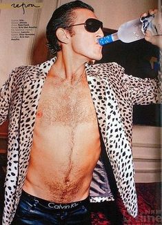 a man with no shirt drinking water from a plastic bottle while wearing leopard print jacket