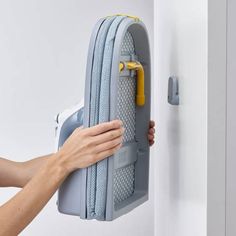 a person holding onto a gray suitcase with yellow handles and latches on the door