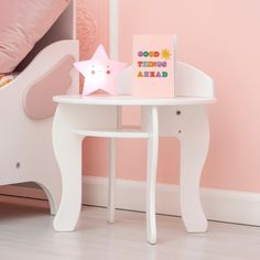 a small white table with a greeting card on it next to a pink wall and bed