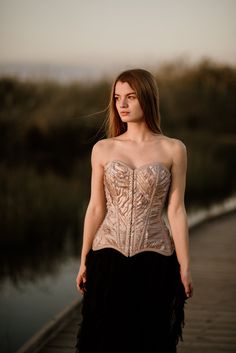 a woman in a corset is standing on a dock by the water at sunset