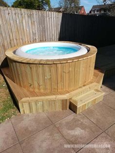 a wooden hot tub sitting in the middle of a yard next to a fence and grass