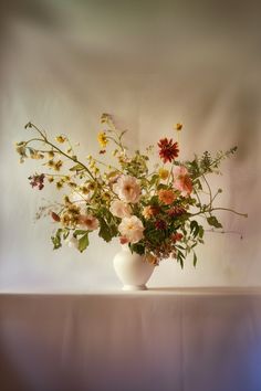 a vase filled with lots of flowers on top of a white tablecloth covered table