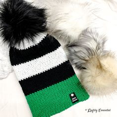 This black and white striped double-layered knit beanie has a green brim and a detachable faux fur pom pom. It looks great with or without a pom, too! This hat is not meant to have a fold-up brim. It does have a bit of slouch. This hat is one size fits most adults. This hat was knitted on a hand-crank circular knitting machine. The faux leather tag and the faux fur pom on this hat are removable. This warm adult beanie is knitted with 100% acrylic yarn. Care instructions: remove pom and set aside Striped Beanie Hat, One Size Fits Most, Striped Beanie Hat One Size, Striped Winter Hats One Size Fits Most, Winter Striped Hats One Size Fits Most, Trendy Black Knit Hat, Green Soft Knit Hat For Cold Weather, Green Knit Beanie For Cold Weather, Cold Weather Green Knit Beanie, Trendy White Knit Hat