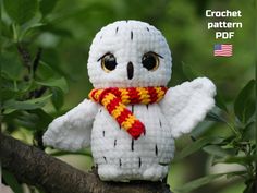 a crocheted white owl with yellow and red scarf sitting on top of a tree branch