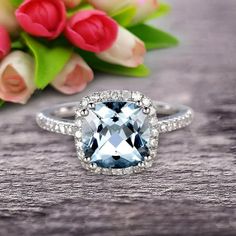 a ring with an aqua blue topazte surrounded by white and clear diamonds sits on a table next to tulips