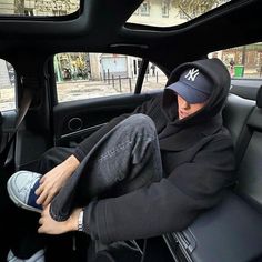 a man sitting in the passenger seat of a car wearing a hoodie and jeans