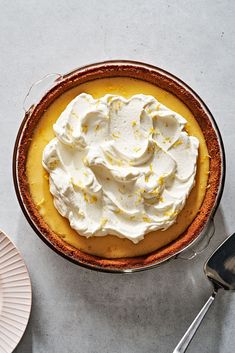 a pie with whipped cream on top sits next to a fork and knife, along with two plates