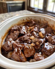 a close up of a bowl of food with meat and onions in it on a table