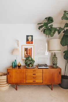 a living room with a plant and pictures on the wall next to a wooden dresser