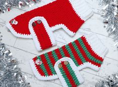 two knitted christmas sweaters sitting next to silver tinsel on top of a wooden floor