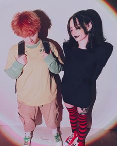 two young women standing next to each other in front of a white wall with a rainbow