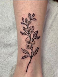 a small black and white flower tattoo on the ankle, with green leaves around it