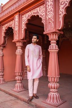 a man standing in front of a pink building with columns and arches on the sides