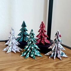 three paper christmas trees sitting on top of a wooden table next to a mirror and wall