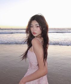 a young woman standing on top of a beach next to the ocean