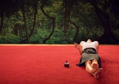 a man laying on the ground in front of a red carpet with trees behind him