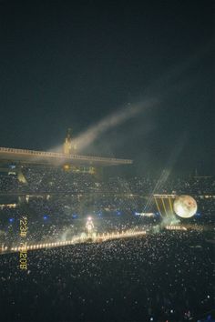 an aerial view of a stadium at night, with lights on the ground and fans in the stands