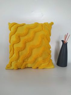 a yellow pillow sitting on top of a white table next to a black vase with sticks in it