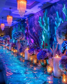 a long table with candles and vases filled with flowers on top of blue cloth