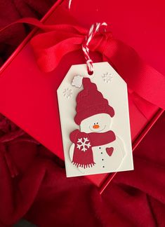 a snowman ornament hanging from a red ribbon on top of a gift bag