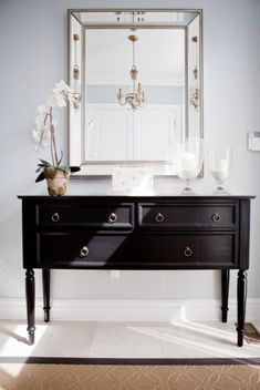 a black dresser with flowers and candles on it in front of a large framed mirror