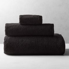 three black towels stacked on top of each other in front of a white wall and floor