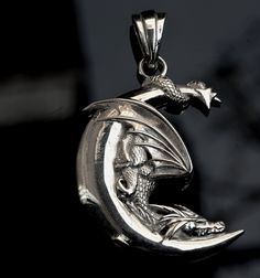 This enchanting silver pendant captures the whimsy of a dragon perched upon a crescent moon. Meticulously crafted, it combines celestial mystery with mythical elegance, offering a unique piece for those who find beauty in the night sky's tales. It's an ideal accessory for dreamers and fantasy lovers alike, providing a touch of magic to any ensemble. Sterling Silver Jewelry With Dragon Design Round Pendant, Round Metal Jewelry With Dragon Design, Sterling Silver Fantasy Jewelry With Dragon Design, Silver Fantasy Jewelry With Round Pendant, Silver Round Pendant Necklace In Fantasy Style, Fantasy Silver Necklace With Round Pendant, Fantasy Silver Jewelry With Round Pendant, Fantasy Silver Round Pendant Necklace, Dragon Design Metal Jewelry