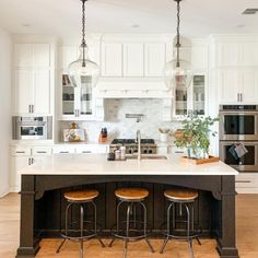 a kitchen island with stools in front of it and three lights hanging from the ceiling