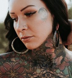 a woman with tattoos on her chest and back is looking at the camera while wearing large hoop earrings