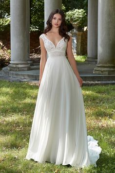 a woman in a white wedding dress standing on the grass near some pillars and columns