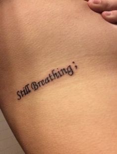 a woman's stomach with the words still breathing tattooed on her lower side ribcage