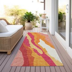 an orange and pink rug sitting on top of a wooden floor next to a white couch